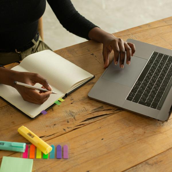 a headless view of someone writing in a notebook next to a laptop